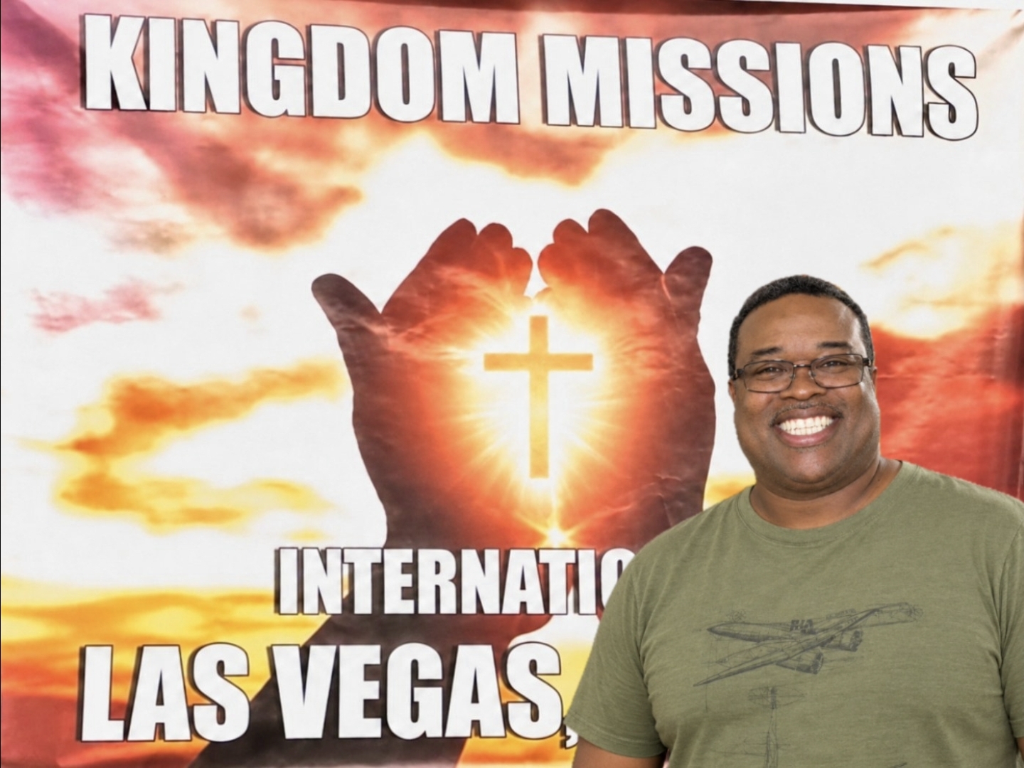 Brother Marc smiling in front of the Kingdom Missions International Las Vegas ministry banner