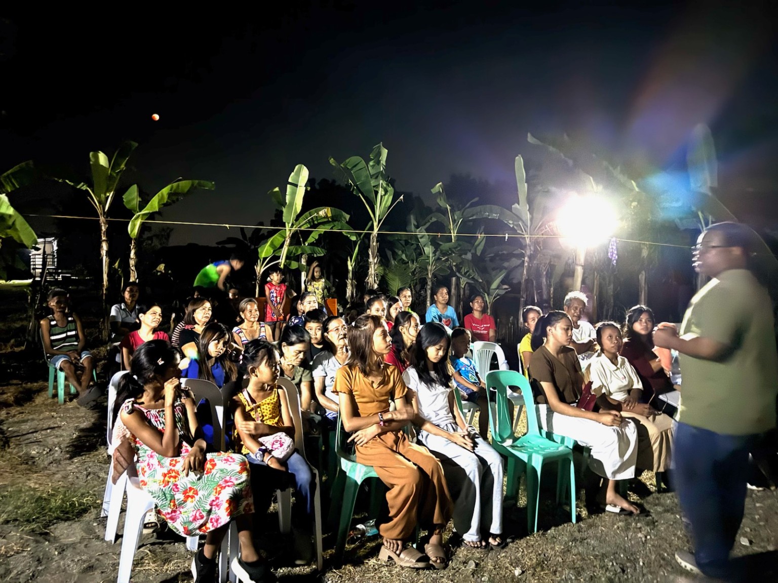 Community members gathered outdoors at night for a KMI ministry teaching session