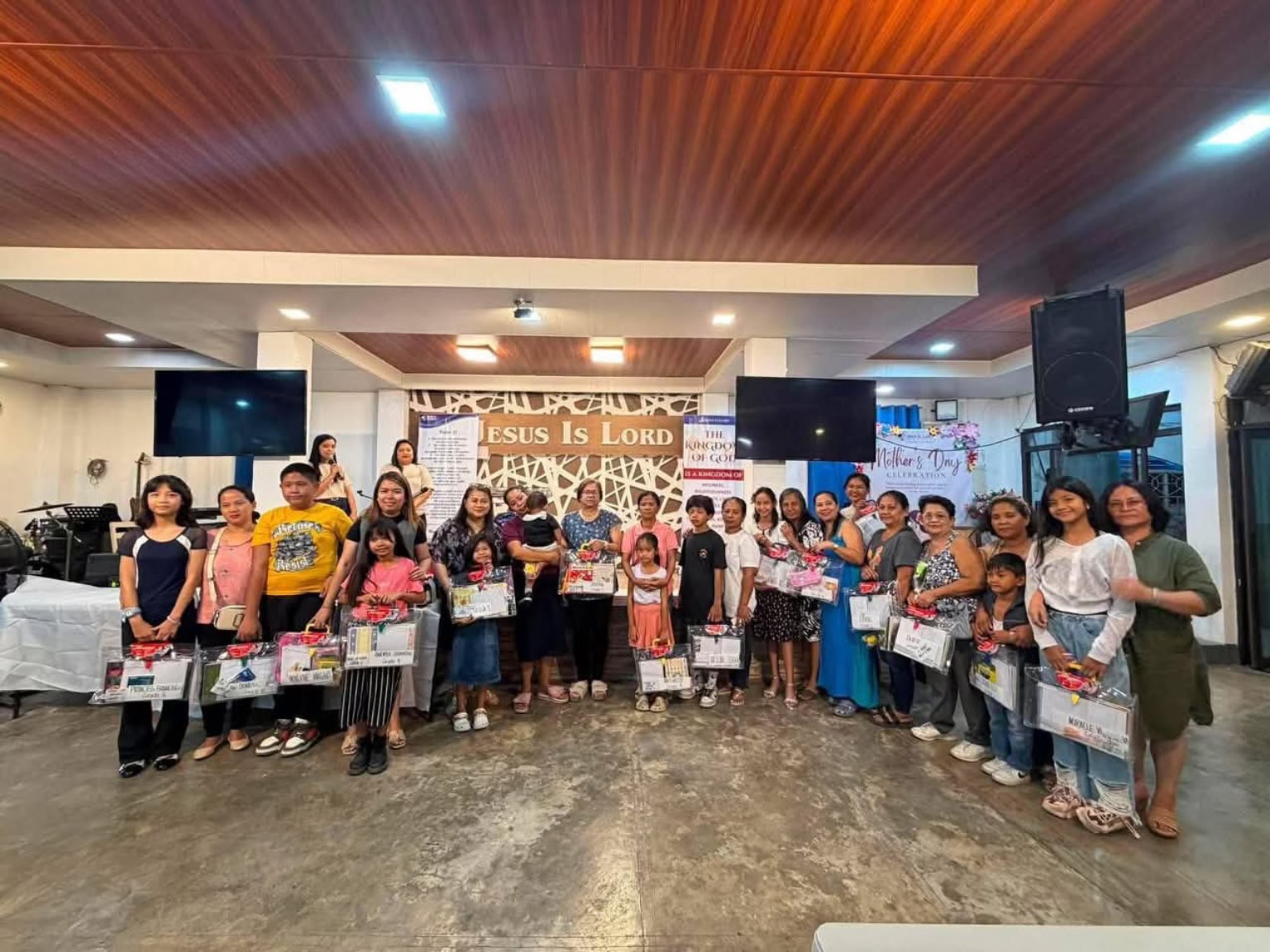 Women and families gathered indoors for a community celebration with gift packages